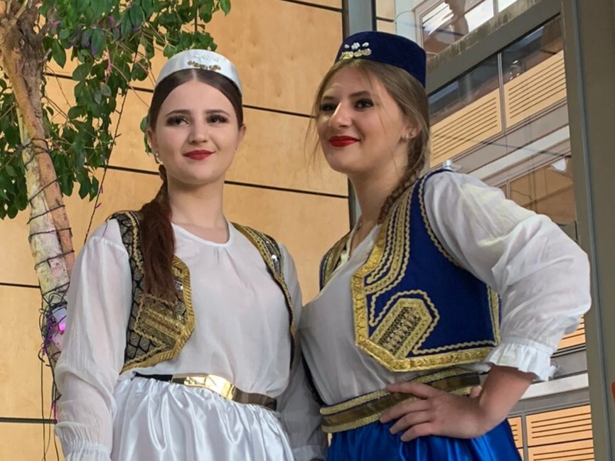 Two young women dressed in traditional costume smile in medium close up